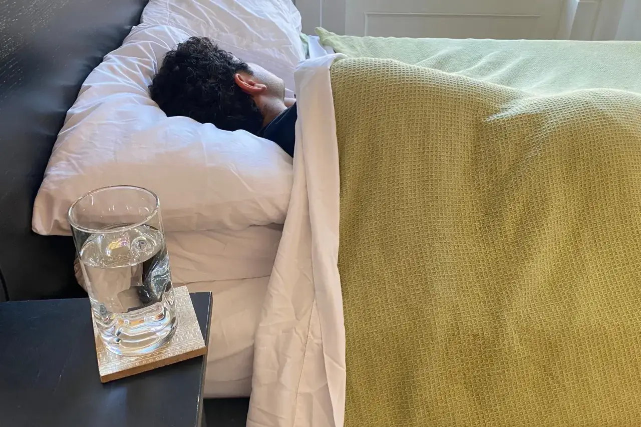 A person sleeps soundly, a glass of water nearby. Is it safe to sleep while dehydrated? This image prompts the question.