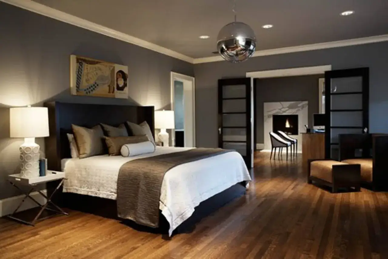 A modern bedroom with a grey color drenching, featuring a large bed, fireplace, and a disco ball hanging from the ceiling.