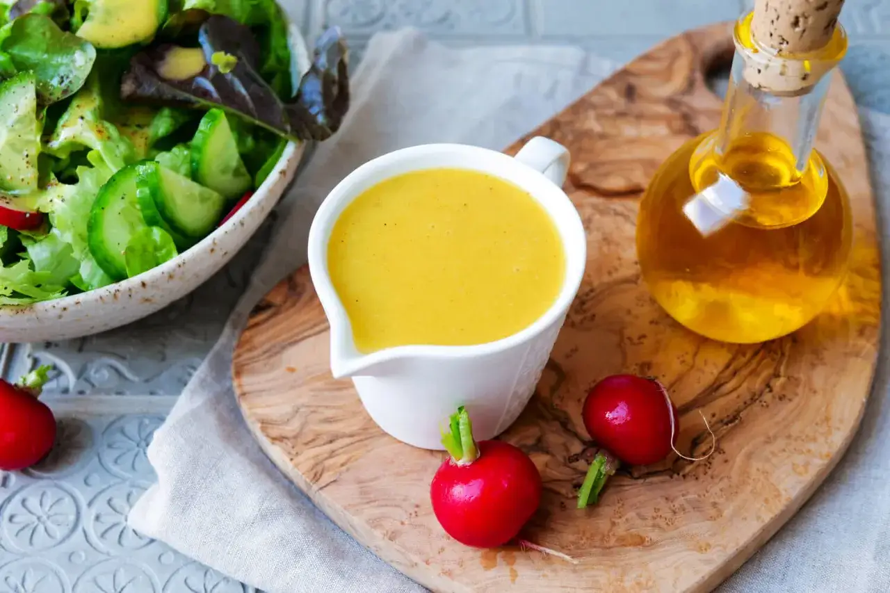 Salat mit Dressing, das mit weißwein essig zubereitet wurde. Daneben eine Karaffe mit Öl und Radieschen.