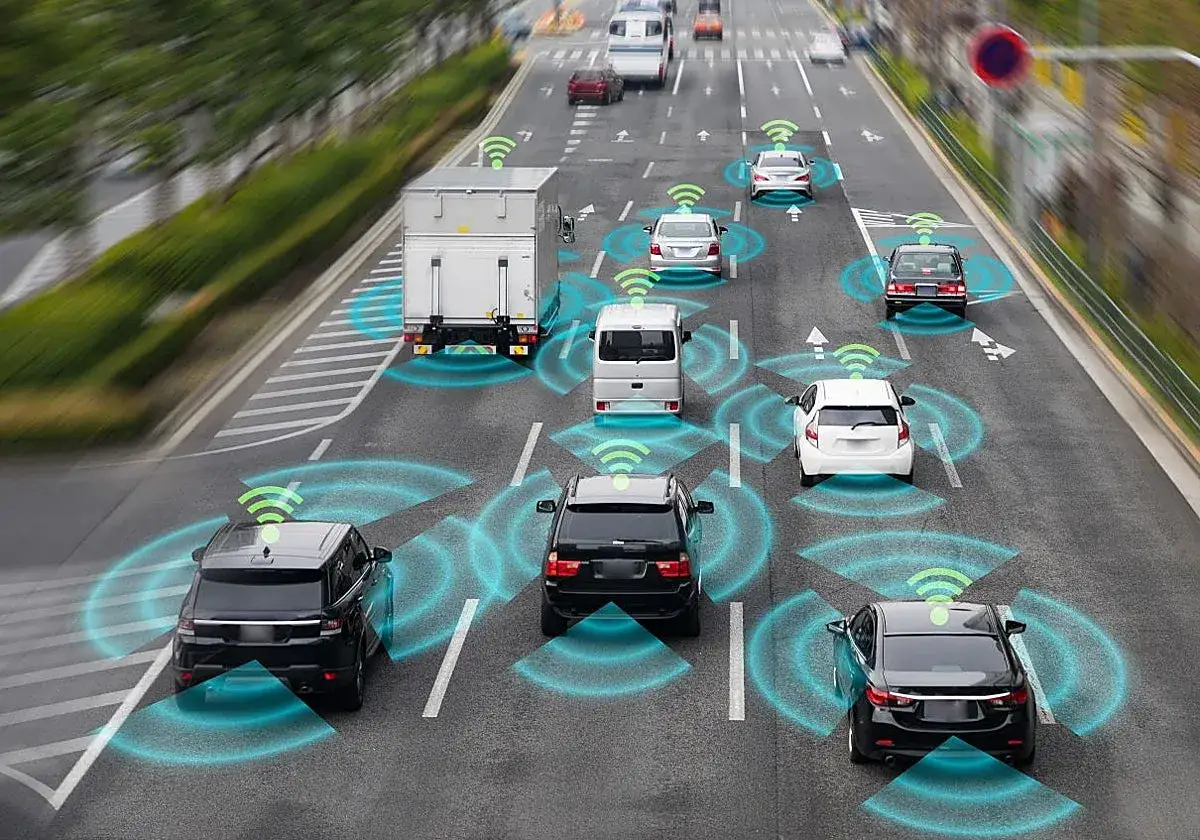 Coches y camiones en una autopista, con ondas verdes indicando la comunicación para la conducción autónoma en España.