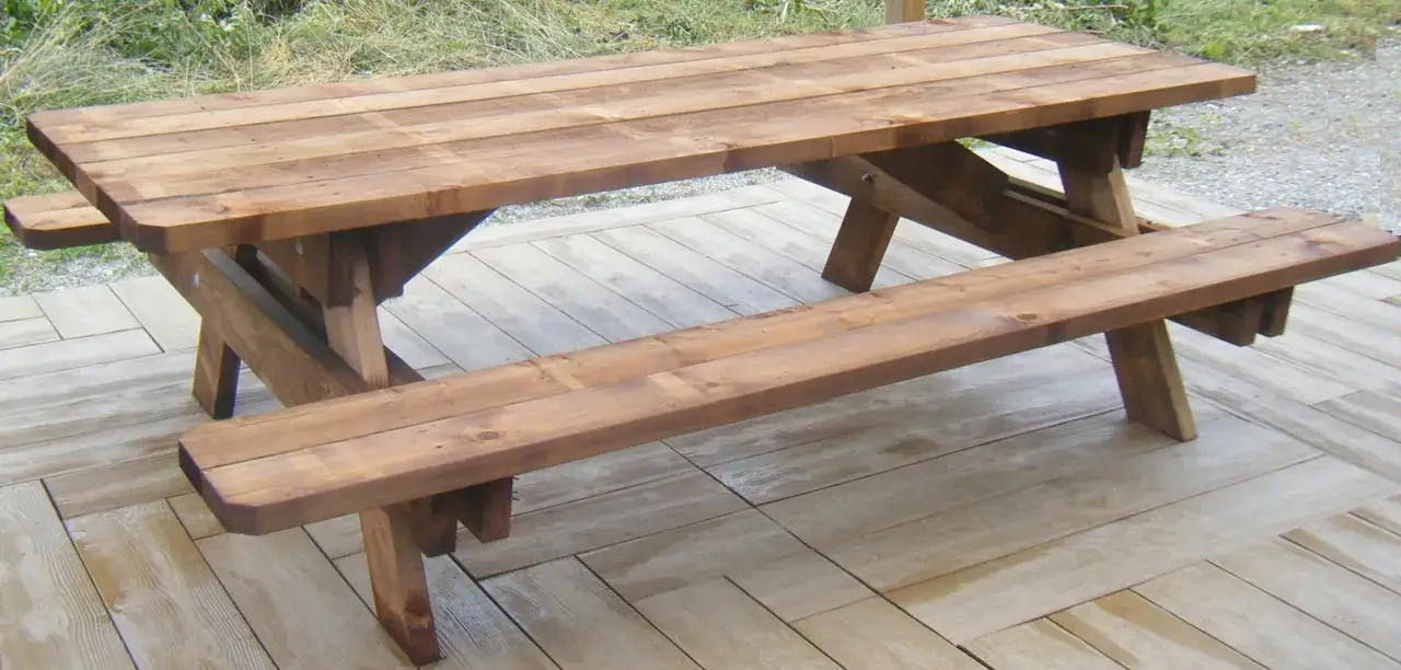 Table en bois ext&eacute;rieur fait maison, avec bancs int&eacute;gr&eacute;s, sur une terrasse en bois. Parfait pour les repas en plein air.