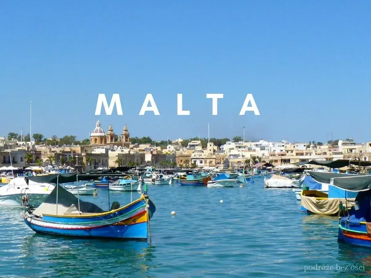 Malta, wrzesień. Słoneczna pogoda nad zatoką pełną kolorowych łodzi rybackich. W tle miasto z kopułami kościołów.