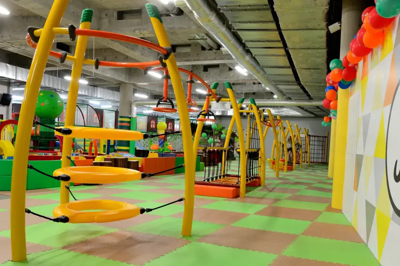 Kolorowa, wielopoziomowa sala zabaw z żółtymi konstrukcjami i zieloną podłogą. Idealne miejsce na dziecięce szaleństwa w Fun Arena Gdańsk.