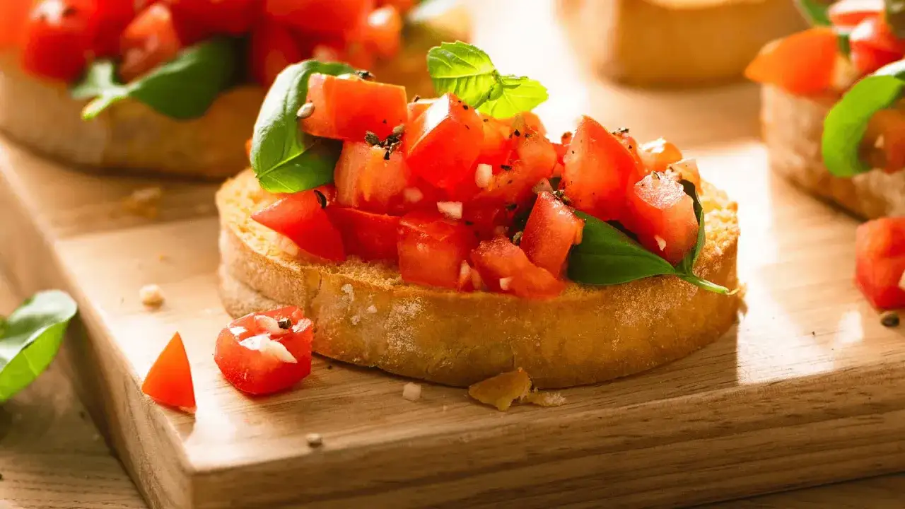 Frisches Bruschetta Rezept: ger&ouml;stetes Brot mit Tomatenw&uuml;rfeln, Basilikum und Knoblauch, auf einem Holzbrett serviert.