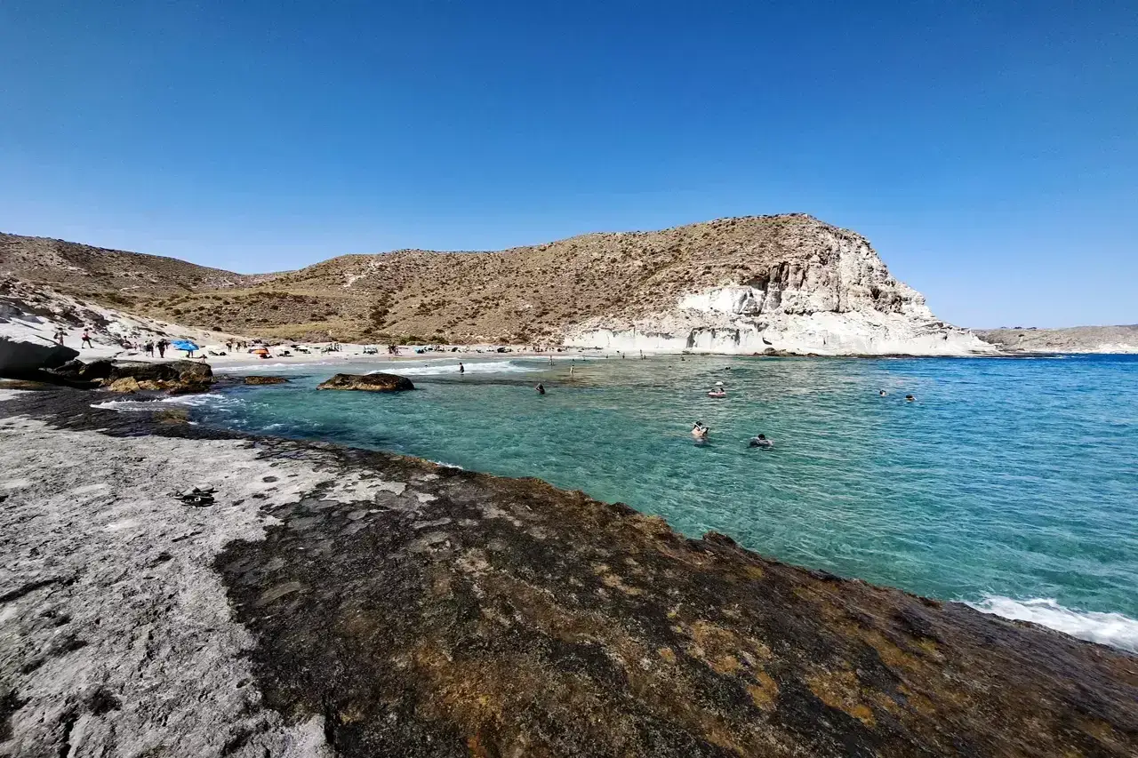 Gente disfruta del sol y el mar en la **costa amarga**, con aguas cristalinas y formaciones rocosas.