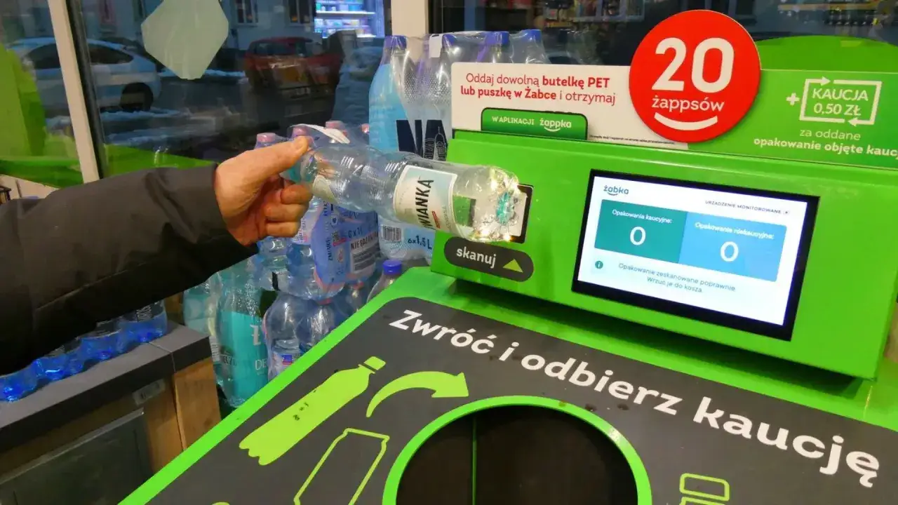 Ręka wrzuca butelkę do automatu, pokazując skutki wprowadzenia nowych przepisów o opakowaniach zwrotnych w handlu.