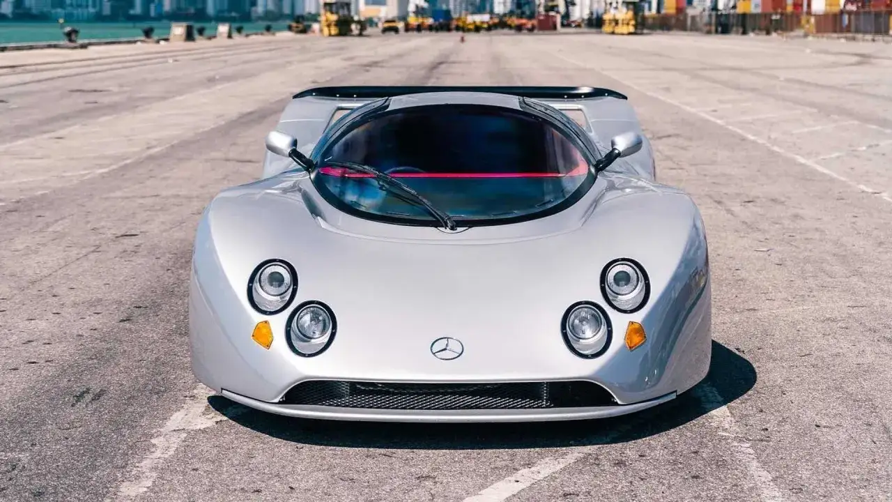 Silberner Lotec C1000 Supersportwagen mit markanten Scheinwerfern und einem roten Streifen &uuml;ber der Windschutzscheibe steht auf Asphalt.