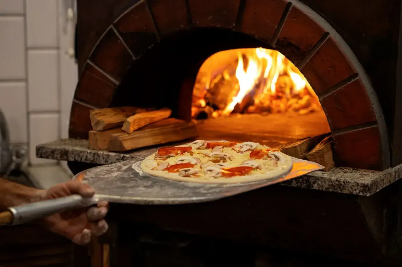 Pizzeria Stare Miasto: pizza z pieca opalanego drewnem, z pomidorami i pieczarkami, gotowa do pieczenia.