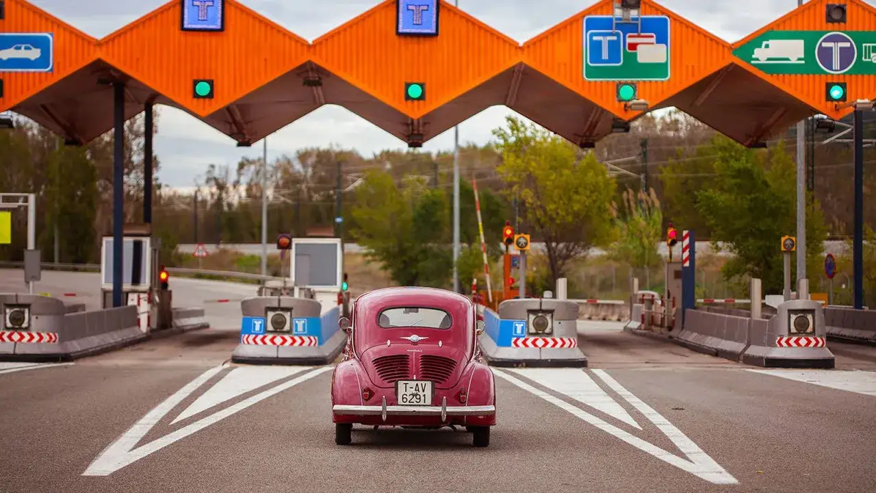 Un coche cl&aacute;sico rosa se acerca a una estaci&oacute;n de peaje. Las luces verdes indican que el sistema de pago funciona.