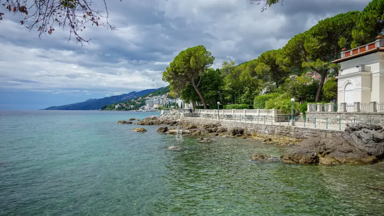 Kamienista plaża i turkusowe morze w Chorwacji. Spacerując promenadą, odkrywasz urokliwe istria atrakcje, w tym zabytkową willę i bujną zieleń.