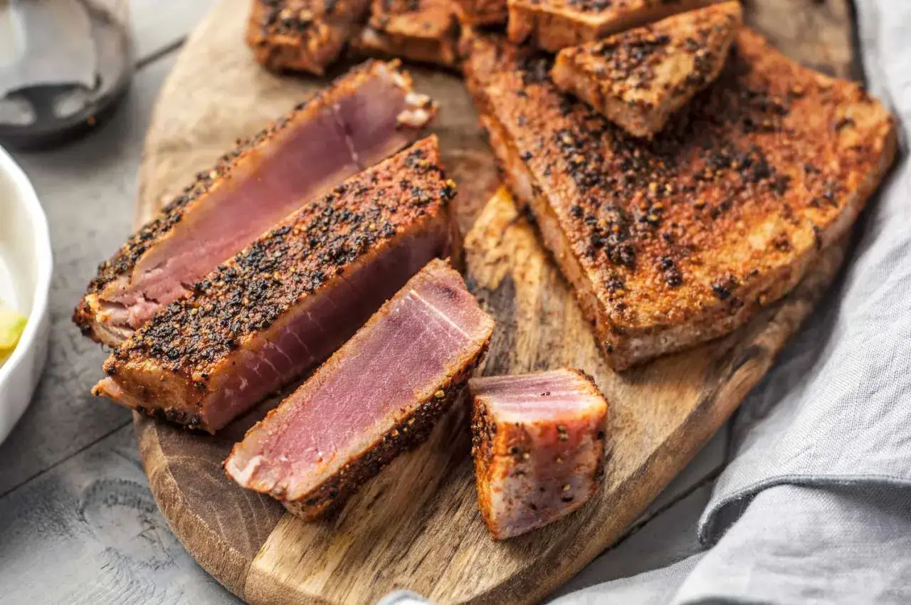 Saftiges Thunfischfilet, perfekt angebraten und mit Gew&uuml;rzen verfeinert, liegt auf einem Holzbrett.