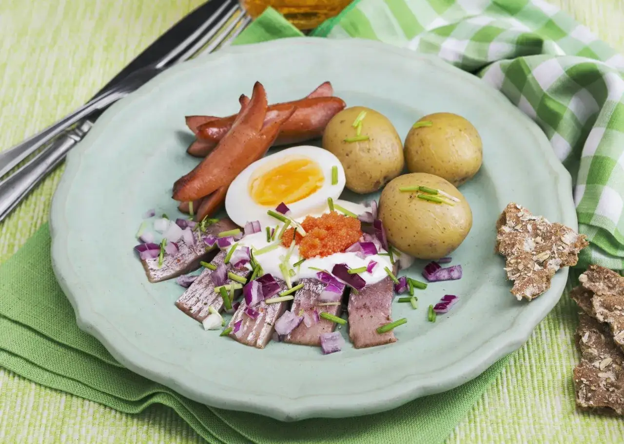 En tallrik med sill, &auml;gg, korv, potatis och rom. En h&auml;rlig p&aring;skbord mat som ser uts&ouml;kt ut.