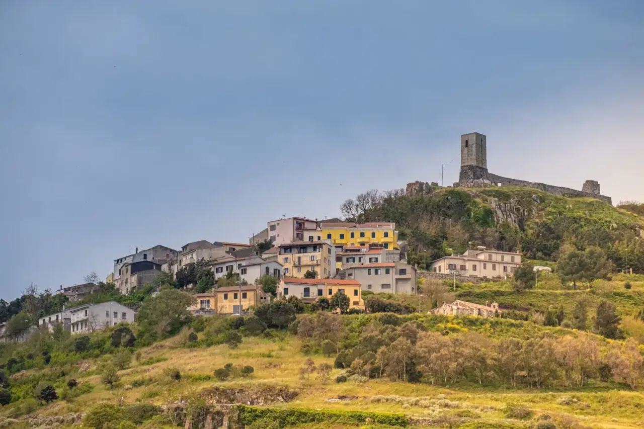 Il castello di Osilo domina un borgo colorato arroccato su una collina verdeggiante, sotto un cielo azzurro.