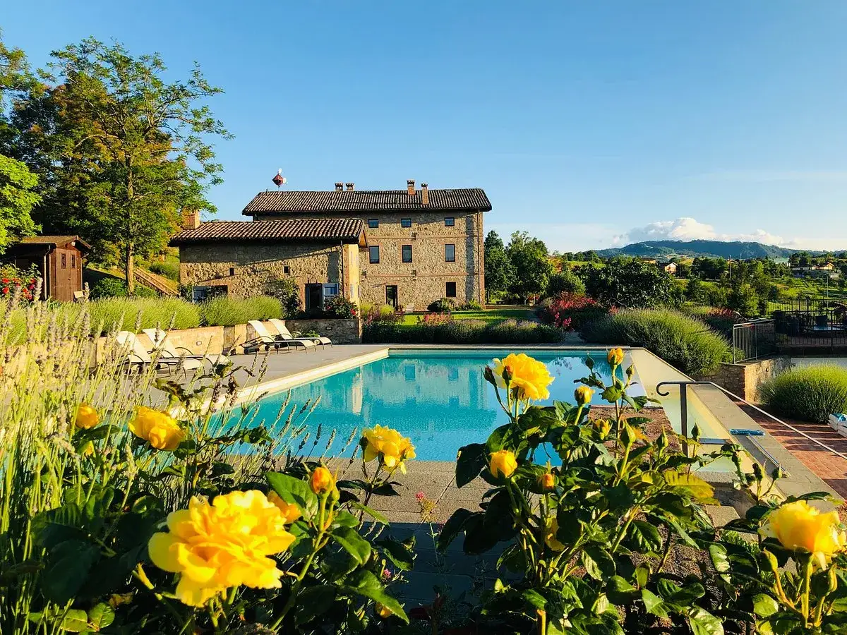 Piscina con vista panoramica, un agriturismo in pietra e fiori gialli. Un luogo incantevole tra i tanti posti da visitare in Emilia Romagna.