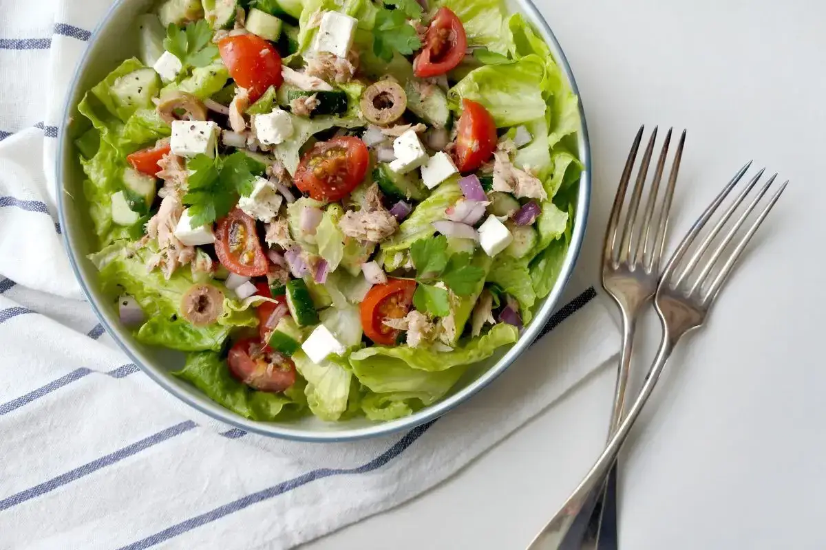 Insalata con feta e tonno, pomodorini, cetrioli e olive. Fresca e colorata, pronta per essere gustata con due forchette d'argento.