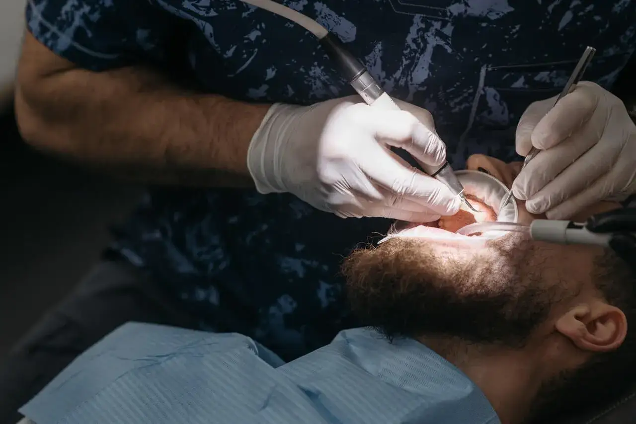 Dentysta pracuje nad zębem pacjenta. Opatrunek na ząb wypadł, więc potrzebna jest pilna interwencja.