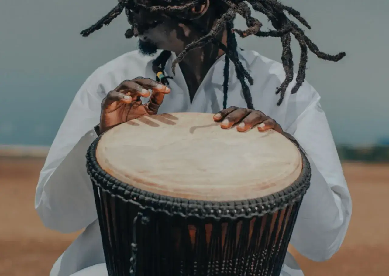 Uomo con dreadlocks suona un djembe, evocando la vibrante musica africana.