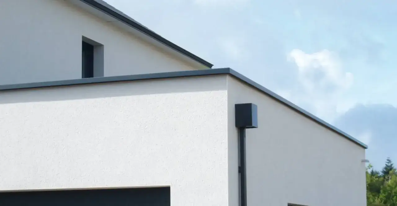 Détail d'une maison moderne avec une gouttière noire et sa fixation couvertine, sous un ciel bleu.