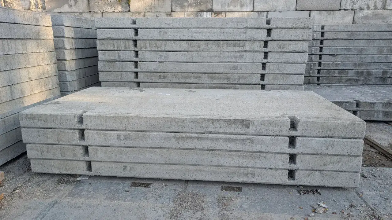 Stos grubych, szarych płyt drogowych betonowych, gotowych do ułożenia na budowie.