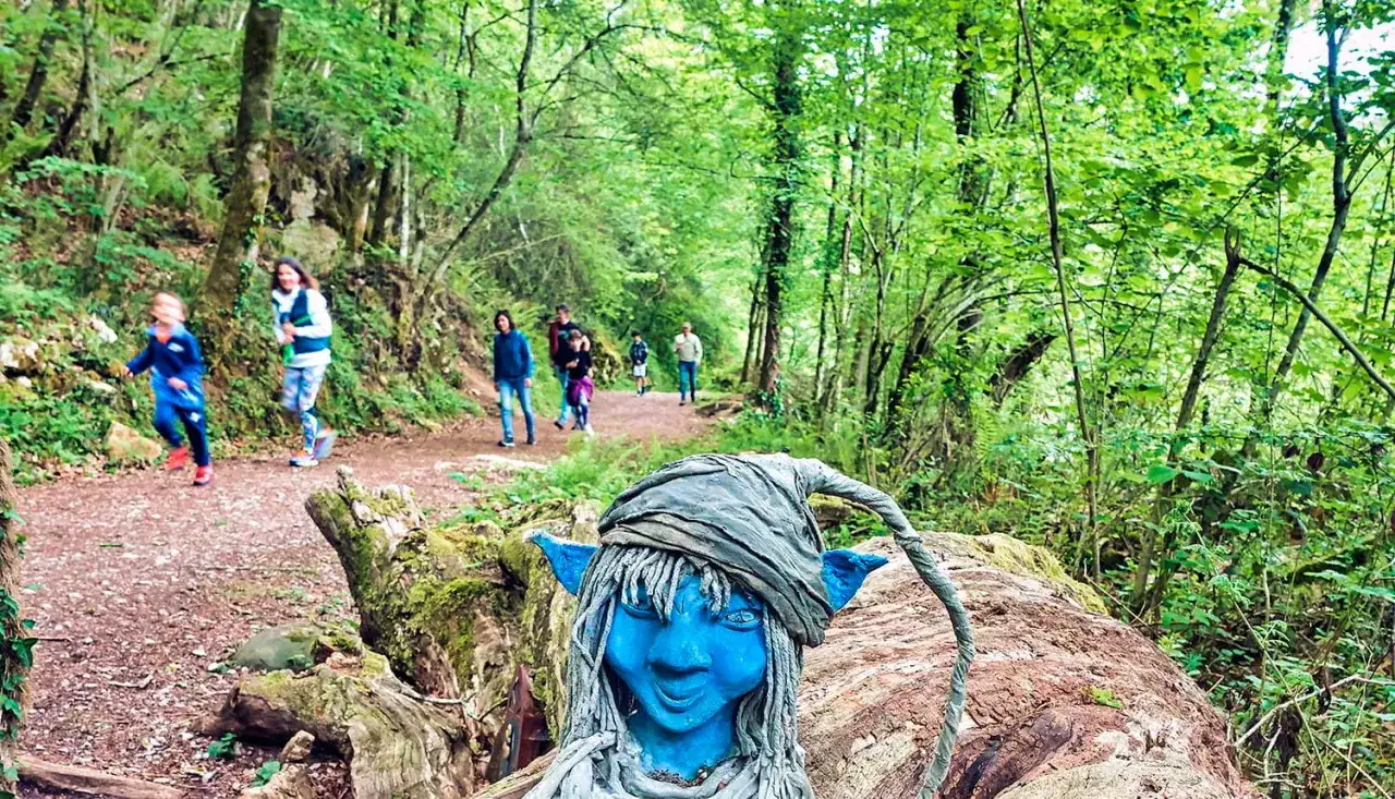 Un duende azul vigila las rutas con niños en Asturias. Familias disfrutan del sendero boscoso.