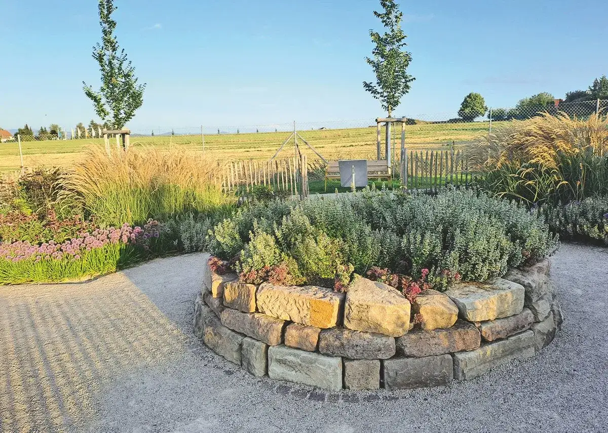 Ein wundersch&ouml;ner natur garten mit einem runden Steinbeet, Ziergr&auml;sern und bl&uuml;henden Stauden.