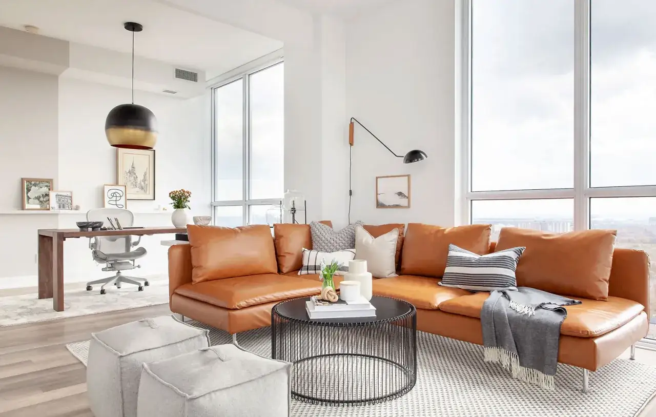 Canapé d'angle en cuir couleur cognac, avec table basse noire, poufs gris et bureau moderne.