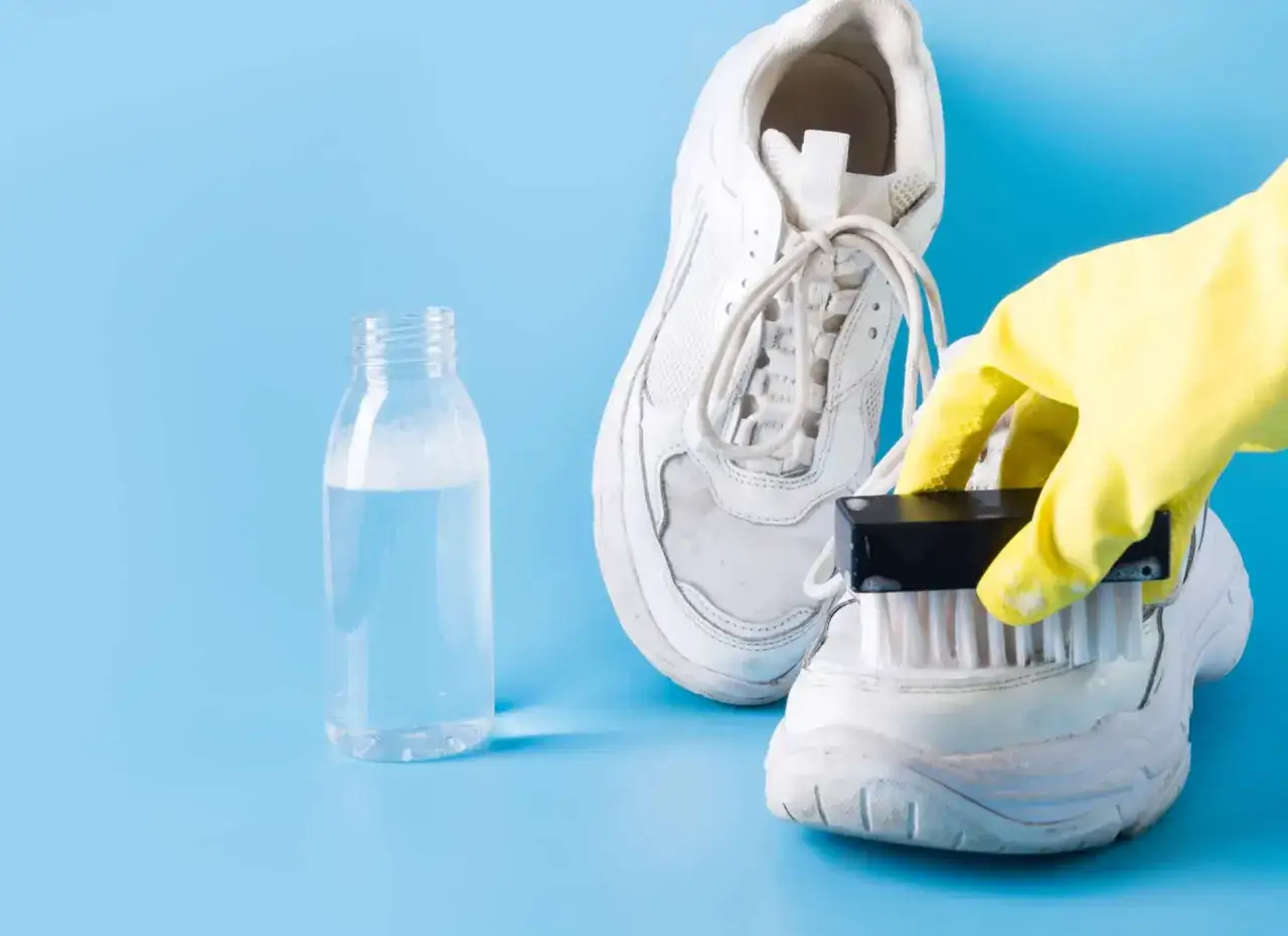 Gelbe Handschuhe reinigen helle Schuhe mit einer B&uuml;rste und einer Flasche Reinigungsmittel.