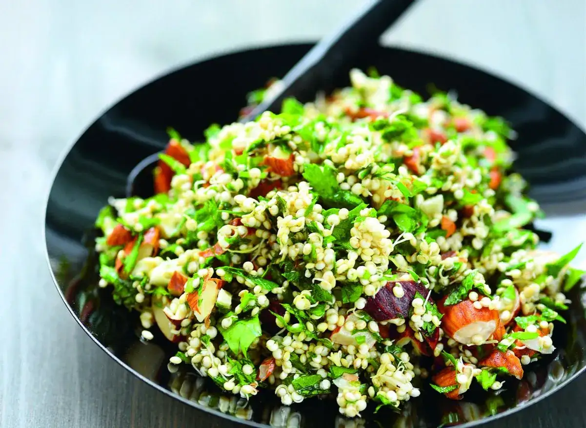 Salade fra&icirc;che et color&eacute;e &agrave; base de germe de quinoa, amandes et herbes vertes, servie dans une assiette noire.