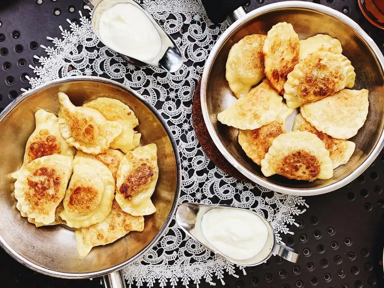 Dwa talerze pełne złocistych pierog&oacute;w, podane z kleksem śmietany. Idealny comfort food na chłodny wiecz&oacute;r.