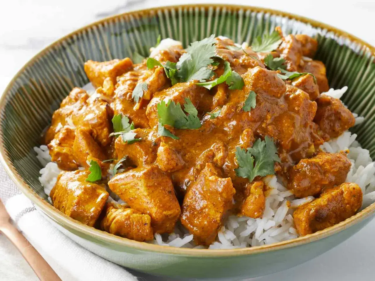 Un delicioso pollo al curry cremoso servido sobre arroz blanco, decorado con cilantro fresco.