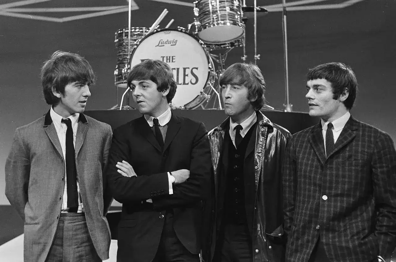 Czterech młodych muzyków, ikony **starych zespołów rockowych**, pozuje przed perkusją z logo The Beatles.