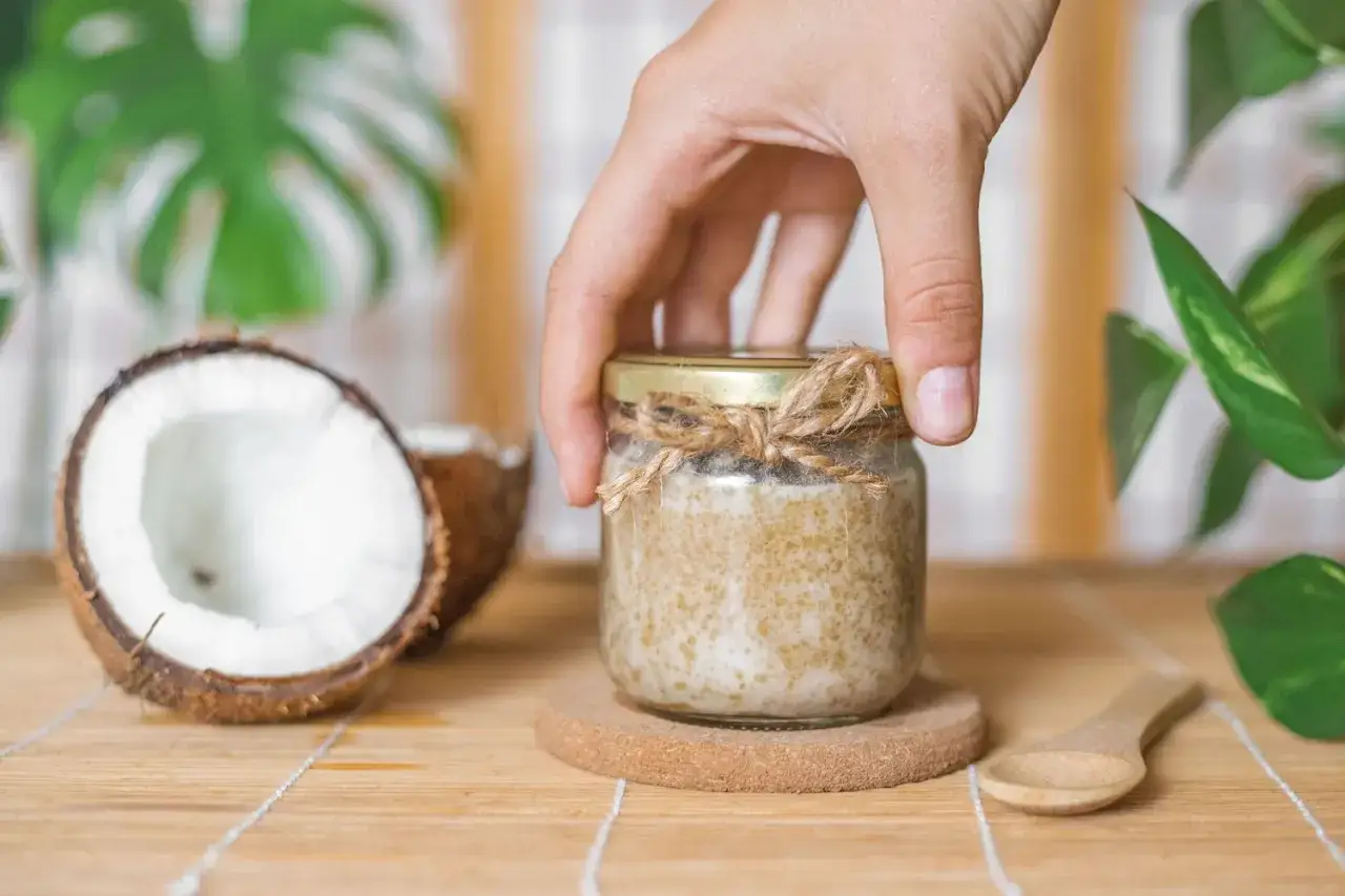 Ein Glas mit selbstgemachtem Kokos Peeling, daneben eine Kokosnuss und ein Löffel.