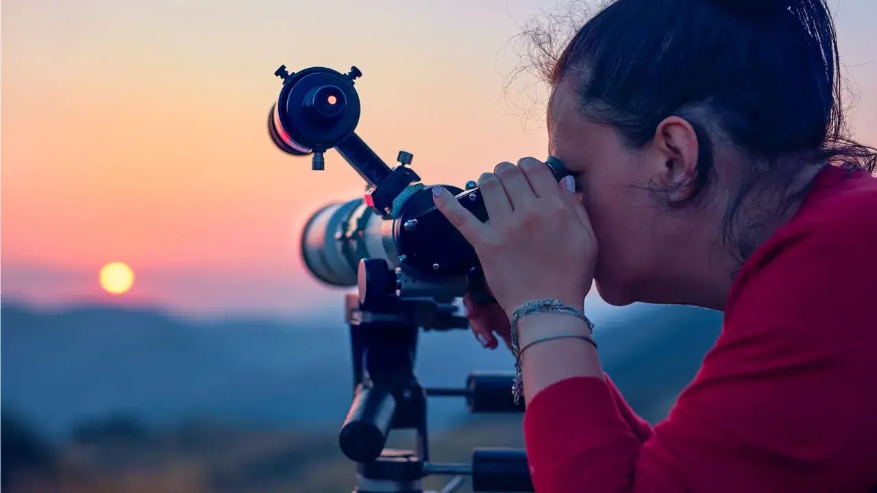 Une femme utilise un télescope pour prendre le soleil en photo lors d'un magnifique coucher de soleil sur les montagnes.