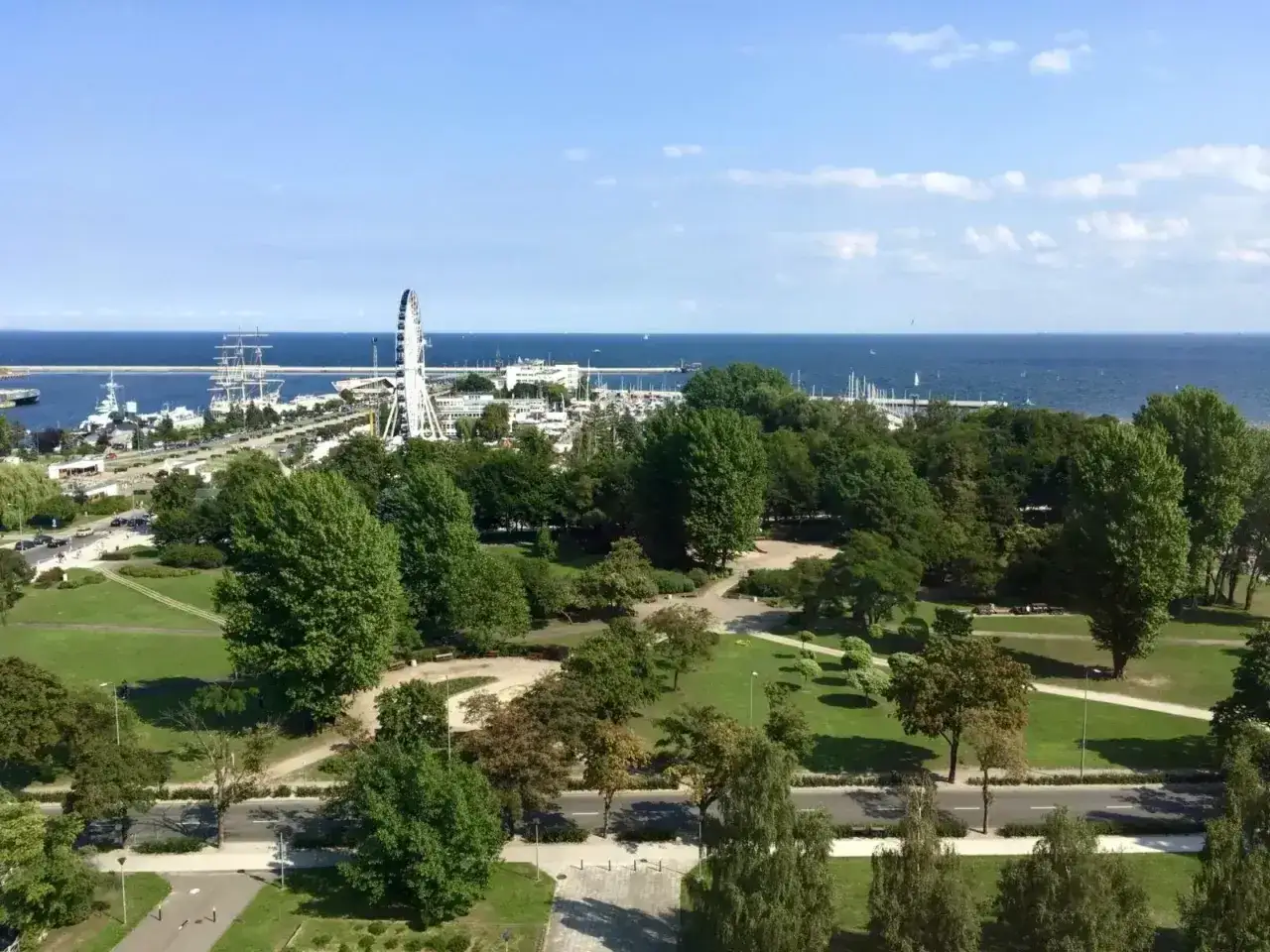 Widok na park, morze i port z żaglowcami. W oddali widoczny diabelski młyn. Hotel Mercure Gdynia w tle.