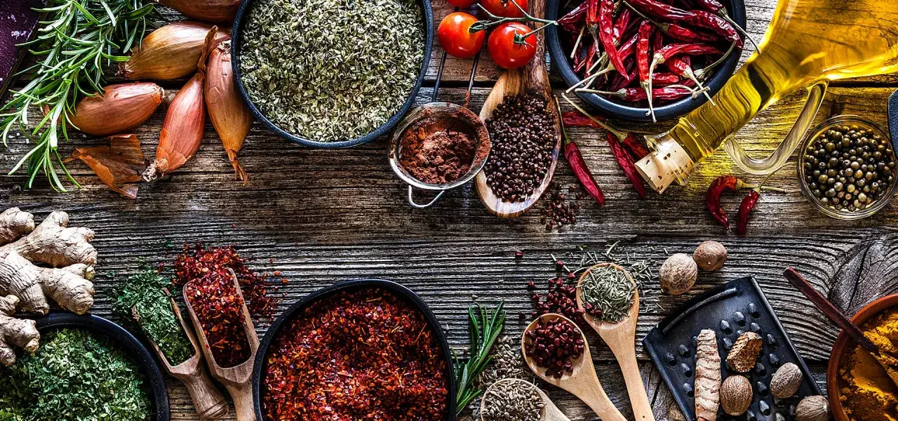 Un ricco elenco spezie indiane: peperoncino, zenzero, curcuma, pepe, rosmarino e altre ancora, su un tavolo di legno rustico.