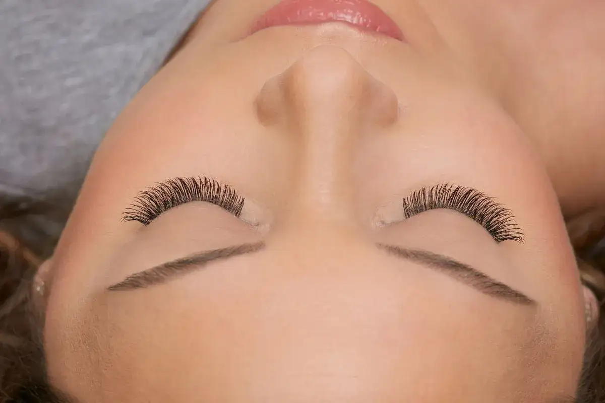 Un gros plan sur les yeux fermés d'une femme, mettant en valeur un maquillage des cils impeccable et des extensions de cils volumineuses.