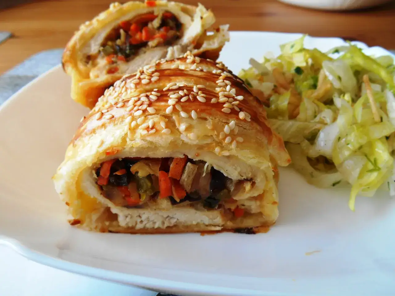 Pyszny kurczak w cieście francuskim z mozzarellą, posypany sezamem, podany z sałatką.