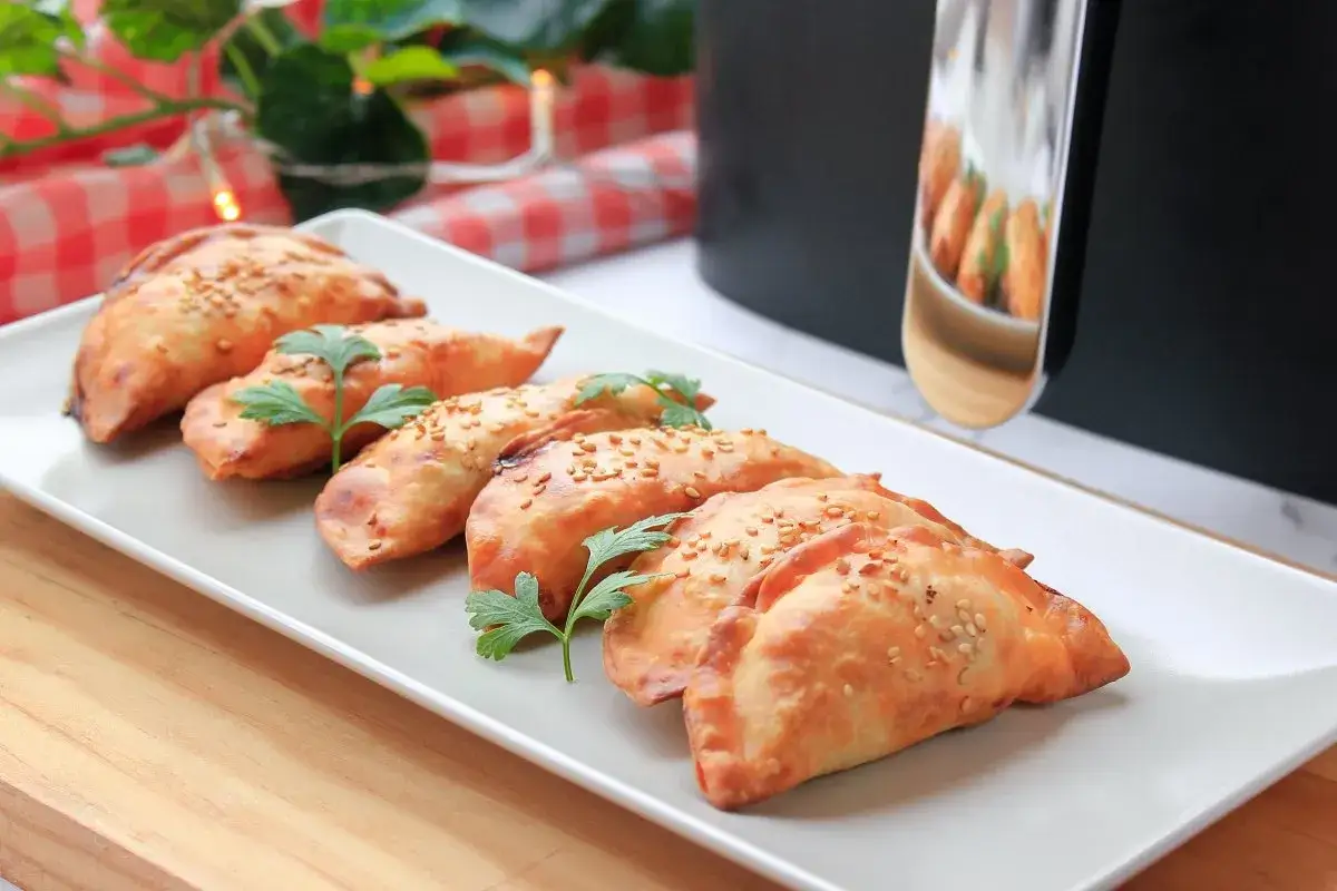 Deliciosas empanadillas en freidora de aire, doradas y crujientes, espolvoreadas con s&eacute;samo y decoradas con perejil fresco.