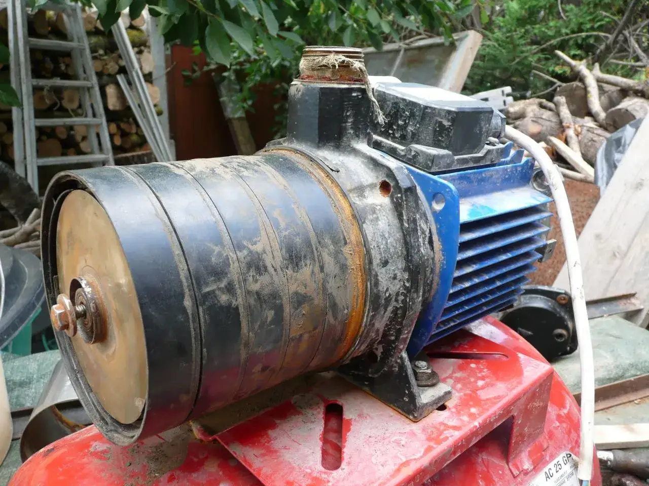 Pompe à eau de jardin sale, prête pour le démontage. Le moteur bleu et le corps noir sont visibles.