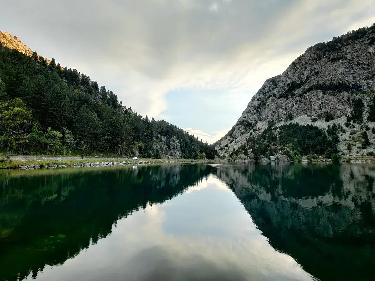 Reflejos perfectos en el ibon de Baños, con montañas cubiertas de pinos y un cielo nublado.