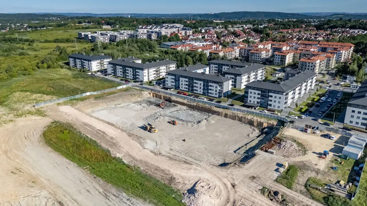 Działka budowlana z maszynami, obok ukończone bloki. Zastanawiamy się, dlaczego deweloperzy wstrzymują inwestycje mimo rekordu mieszkań w budowie.