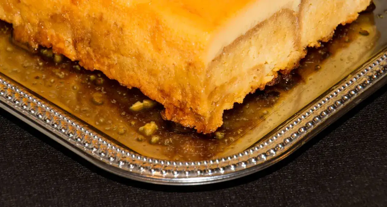 Un trozo de pastel de maiz dorado y húmedo, bañado en un sirope dulce, servido en una bandeja plateada con borde decorado.