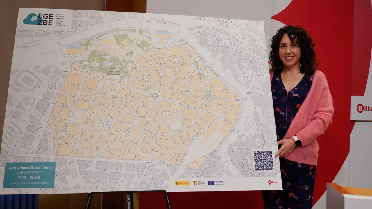 Mujer sonriente presenta mapa de la zona de bajas emisiones (ZBE) de Bilbao, detallando horarios de acceso.