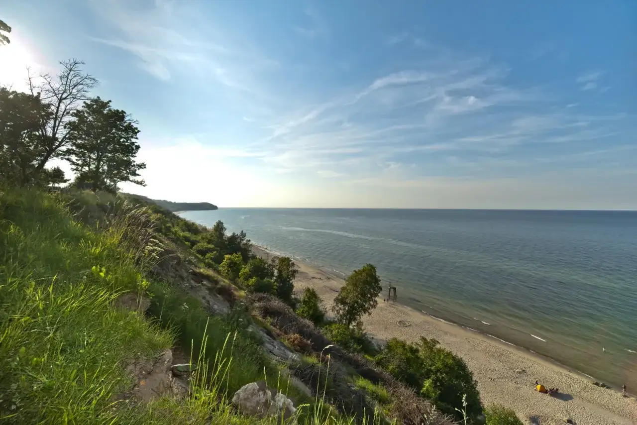 Widok na morze z klifu porośniętego trawą i drzewami. Piękna plaża, idealna na spacer po 