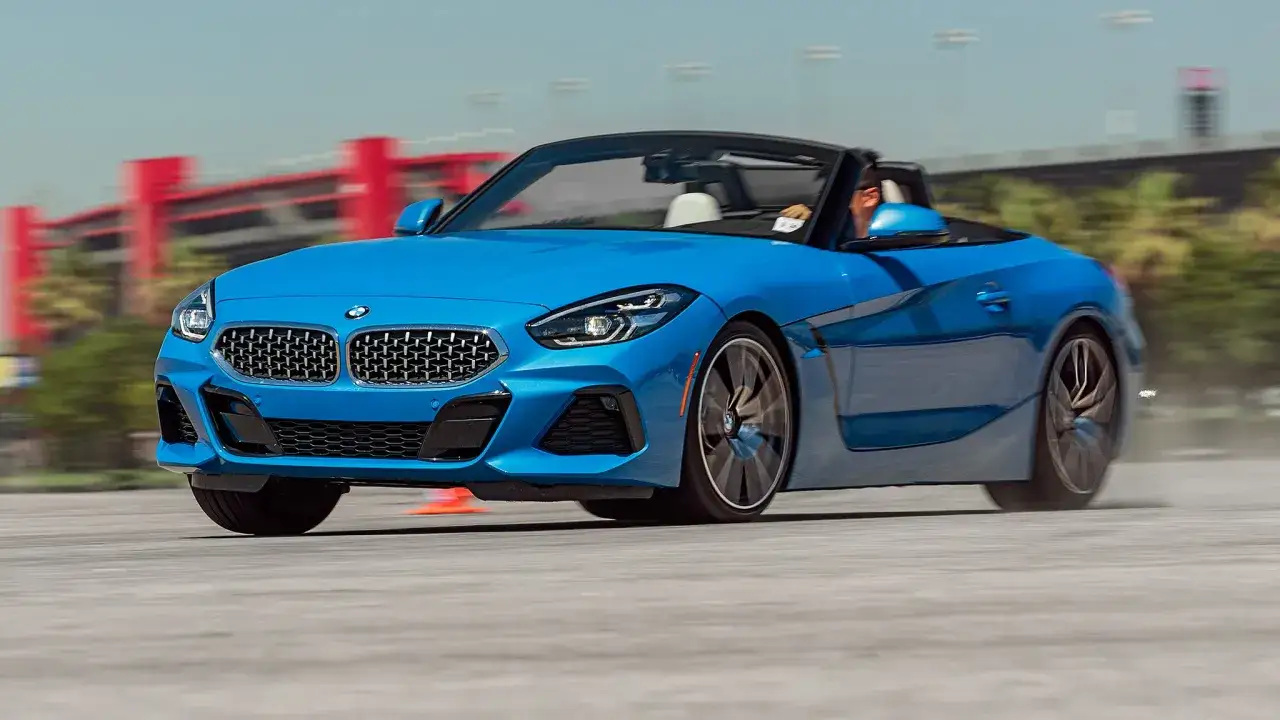 Un BMW Z4 capota dura azul brillante acelera en una pista, con el conductor visible.