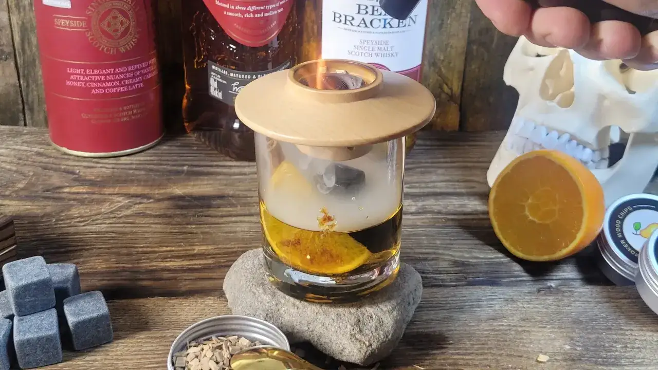 Dymiące drinki z whisky, z pomarańczą i kamieniami do napojów. W tle butelki szkockiej whisky i czaszka.