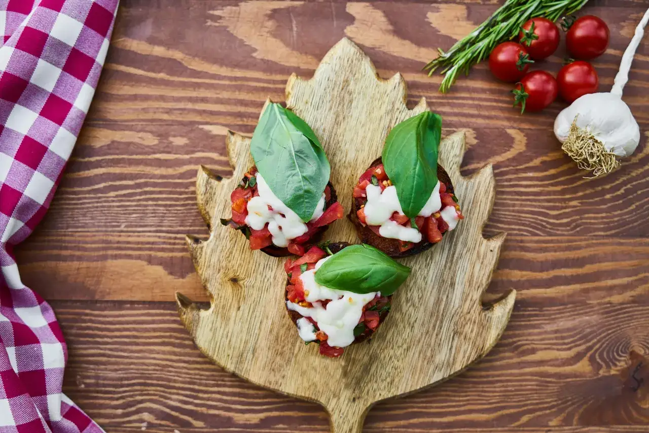 Pyszne bruschetty z pomidorami i mozzarellą na liściastej desce. Idealne, by zainspirować, co ugotować na walentynki.