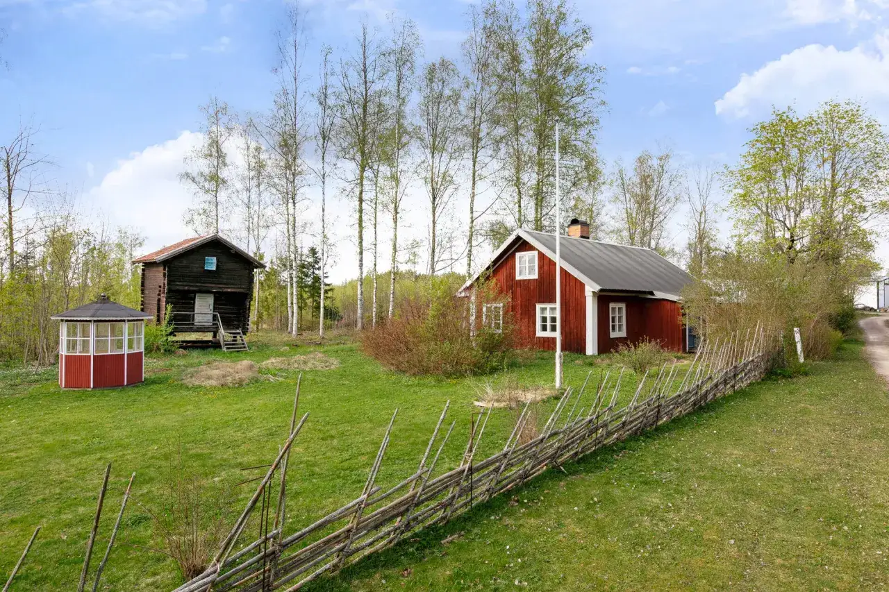 Idylliskt boende i Stjärnsund med röda hus, timmerstuga och lusthus i en grönskande trädgård.