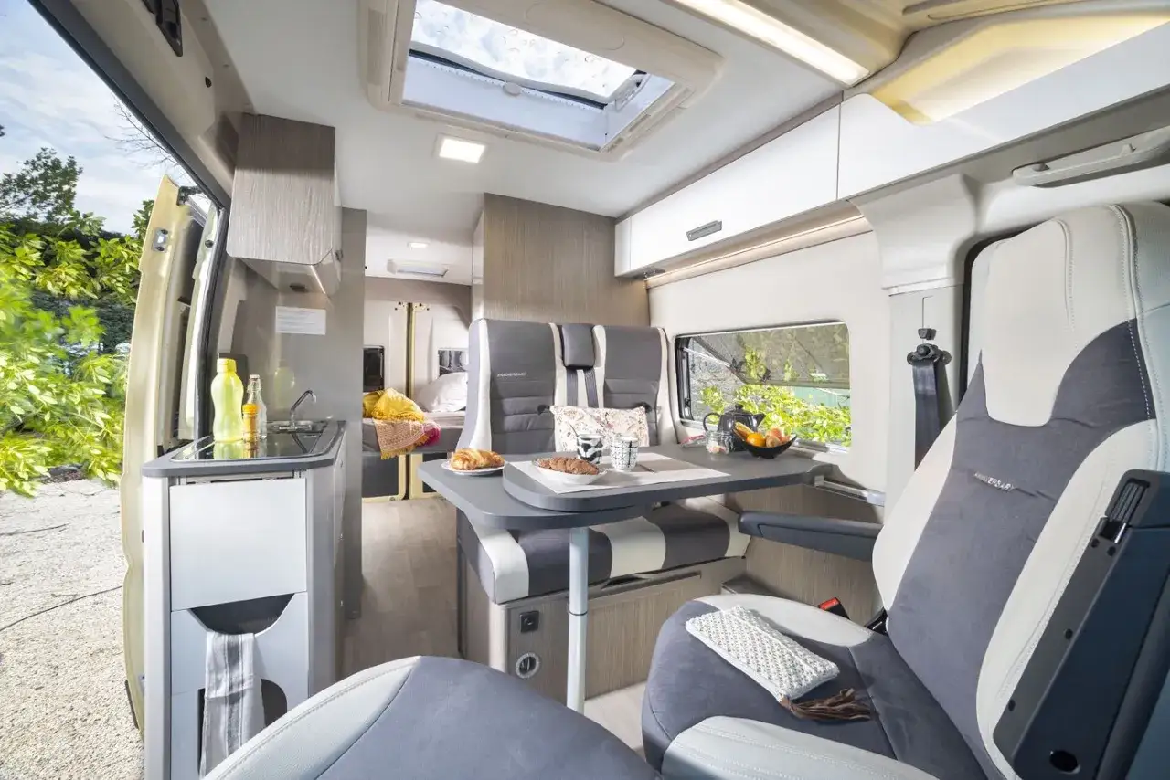 L'intérieur d'un camping-car moderne, idéal pour construire son camping car. Cuisine, coin repas et lit sont visibles.