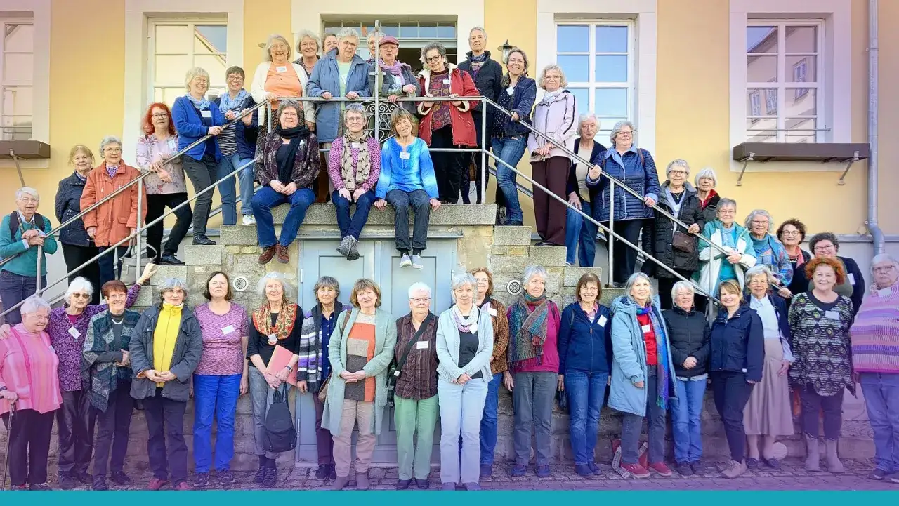 Eine Gruppe von Frauen, die an einer evangelischen Nonnen-Veranstaltung teilnehmen, posiert l&auml;chelnd auf einer Treppe vor einem gelben Geb&auml;ude.